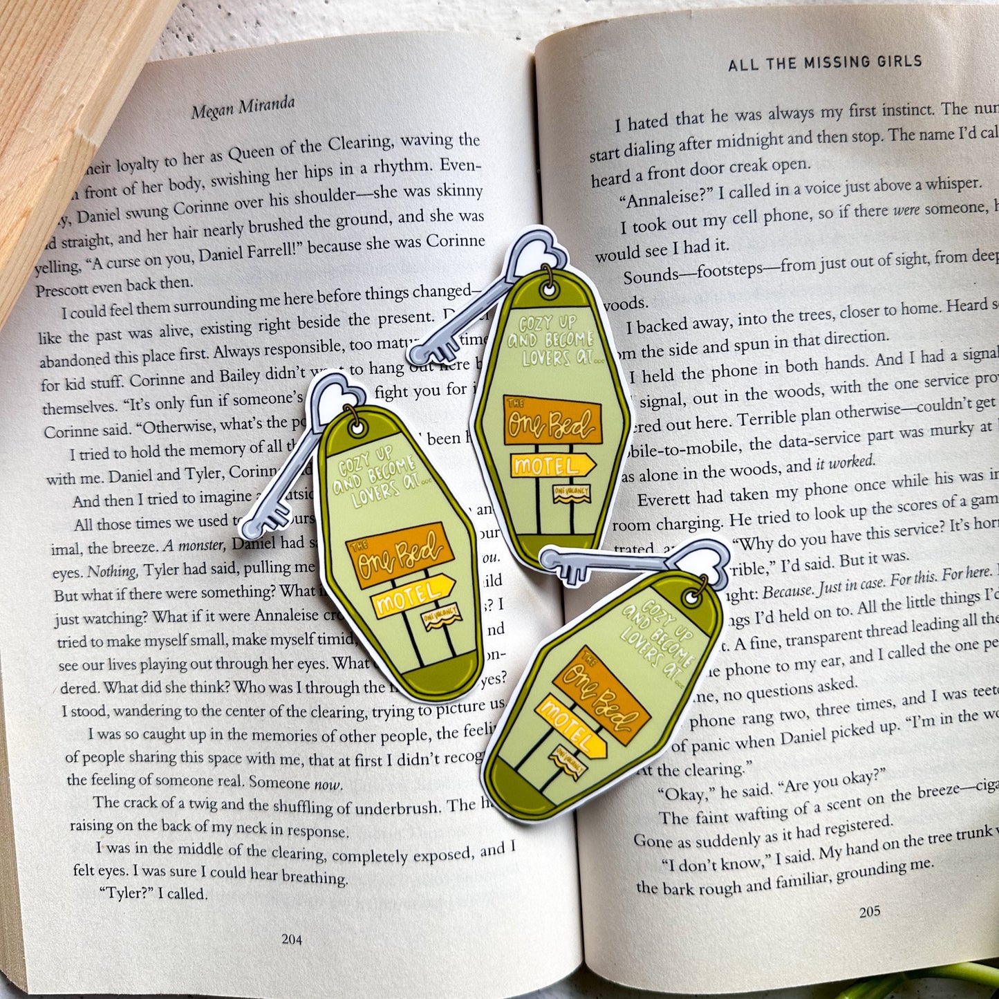 Two green and gold earrings shaped like small houses on an open book.