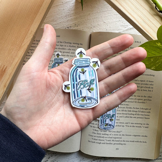 Hand holding a decorative bottle-shaped sticker with 'Bottle' text, placed on an open book.