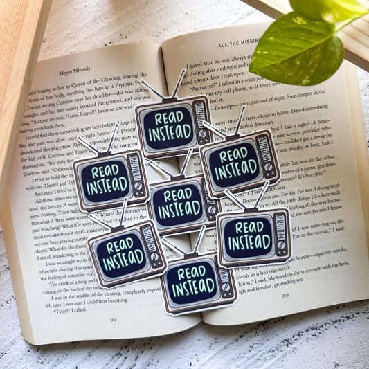 Set of 'Read Instead' stickers on an open book with a plant in the background.