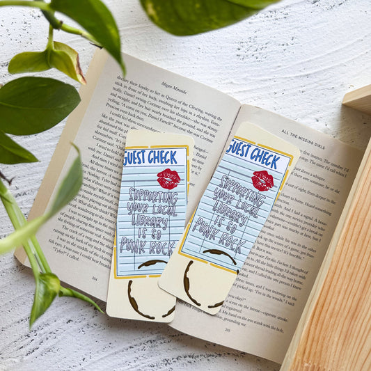Open book with 'Just Check' bookmarks on a wooden surface with a plant.