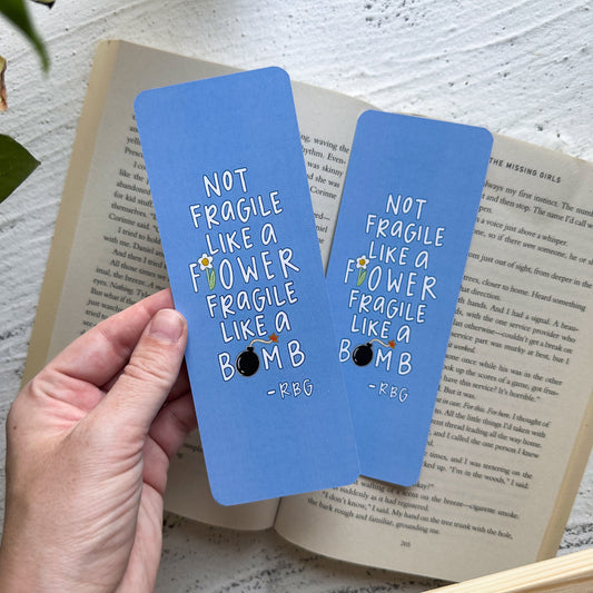 Two blue bookmarks with text held over an open book on a light surface.