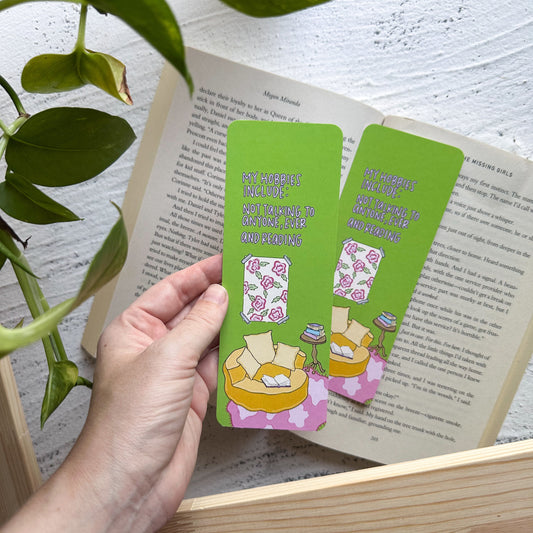 Hand holding green bookmarks with cartoon designs over an open book on a wooden surface.