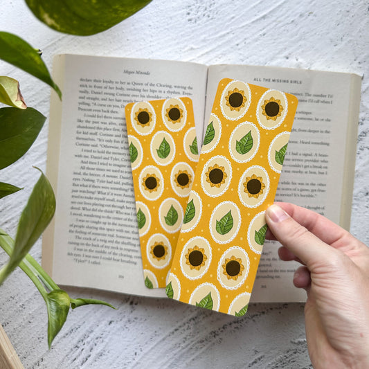 Open book with a sunflower patterned bookmark on a white surface with green leaves.