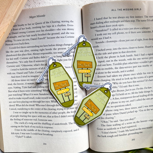 Two green and gold earrings shaped like small houses on an open book.