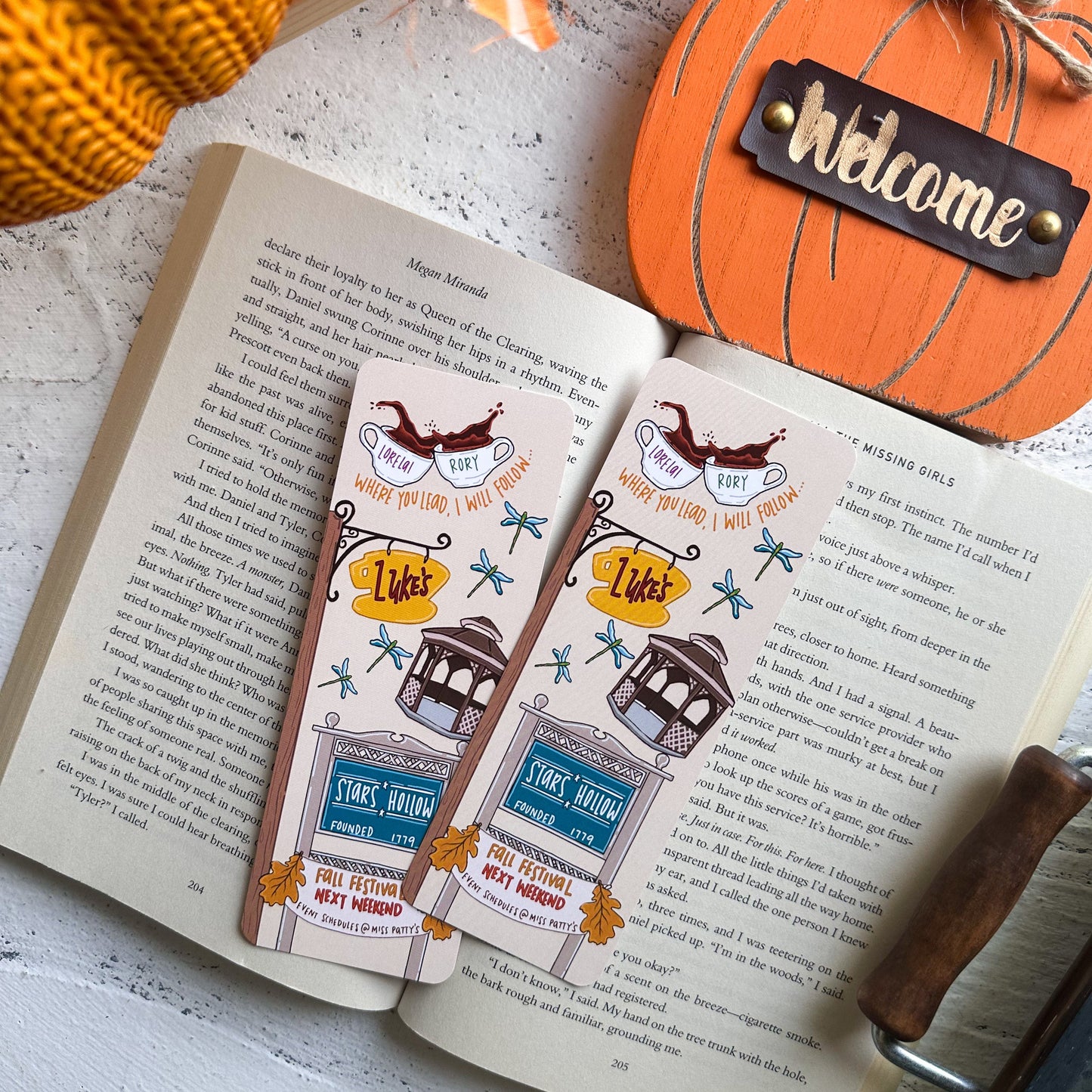 Open book with decorative bookmarks and a small pumpkin labeled 'Welcome' on a wooden surface.